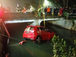 Mobil Honda Jazz merah yang nyemplung ke sungai saat dievakuasi petugas. (Foto: info kedaruratan 112 Surabaya)