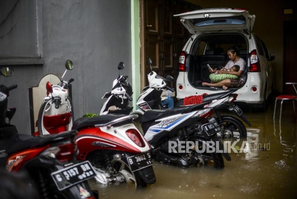 Seorang warga duduk diatas mobil bersama anaknya saat tergenang banjir di kawasan Jatipadang, Pasar Minggu, Jakarta, Rabu (1/1). (Foto: Republika/Putra M. Akbar)