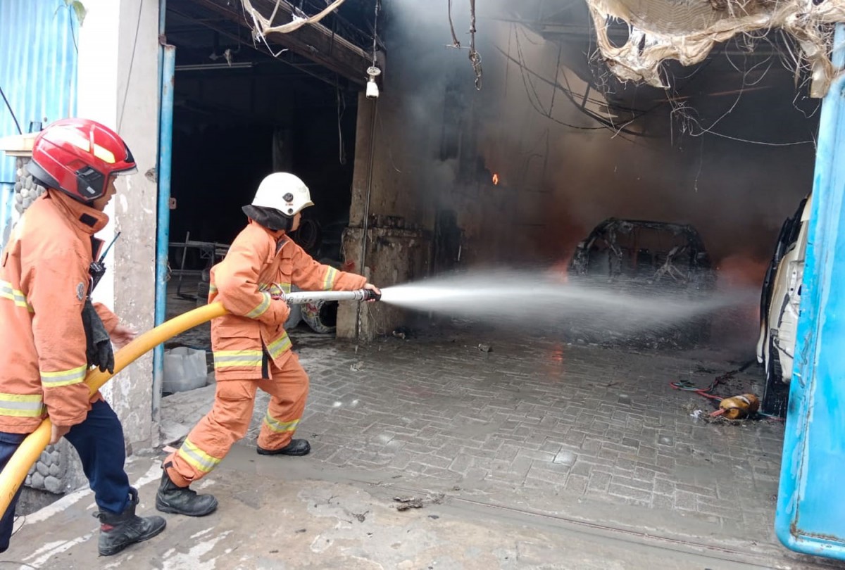 Petugas memadamkan api yang membakar mobil dalam bengkel