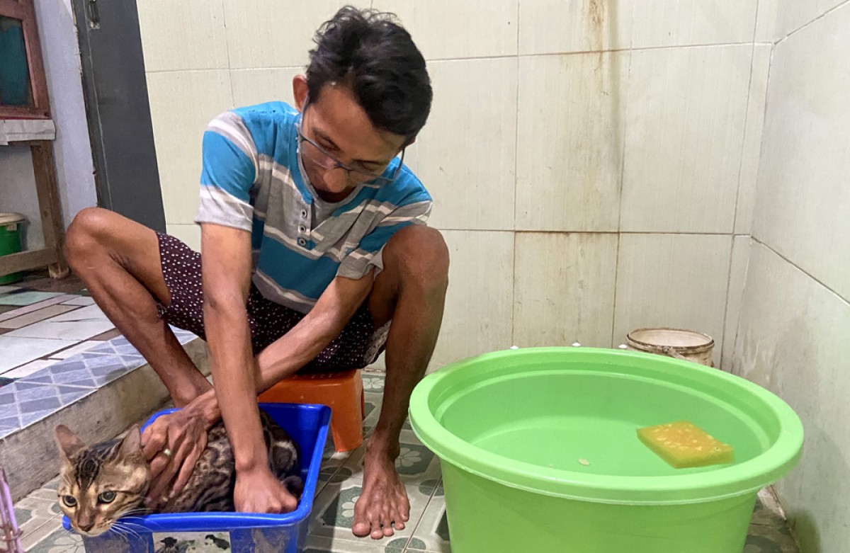 Iphied saat memandikan kucing milik salah satu pelanggannya. (foto: Mita Kusuma/jatimnow.com)