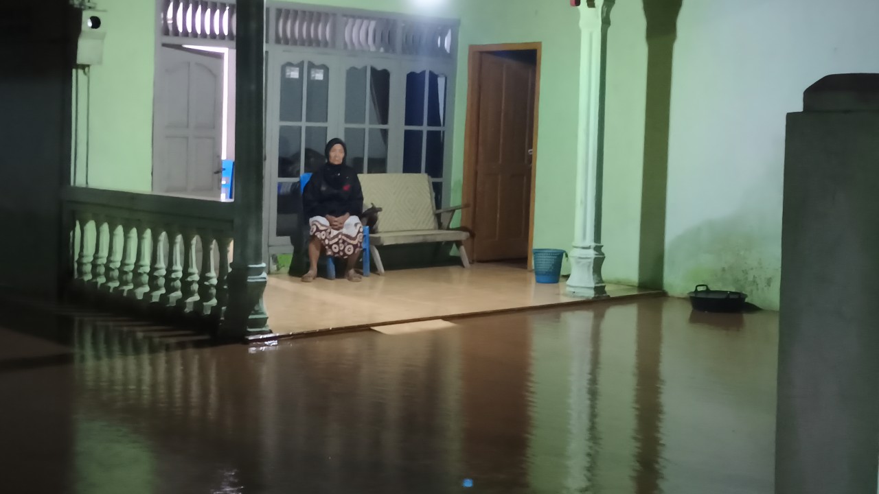 Nenek di Desa Sumberarum yang menanti genangan banjir surut di teras rumah.