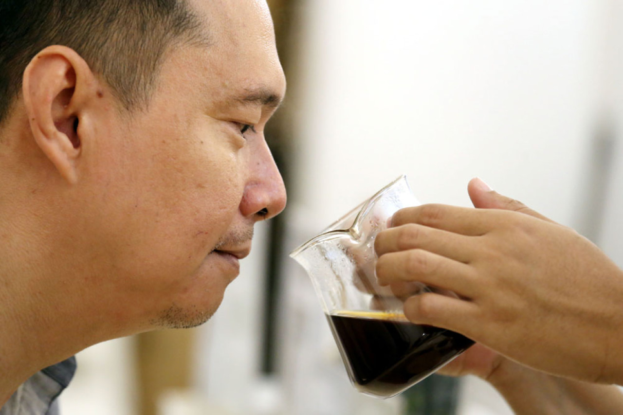Penikmat kopi menghirup aroma kopi racikan barista di Cafe Drama Roastery, Jl. Tunjungan Surabaya, Jawa Timur, Senin (04/8/2025). Cafe berjejaring ini merupakan salah satu pengguna kopi Arabika dari Lereng Gunung Arjuna. Foto: Ali Masduki/JatimNow.com