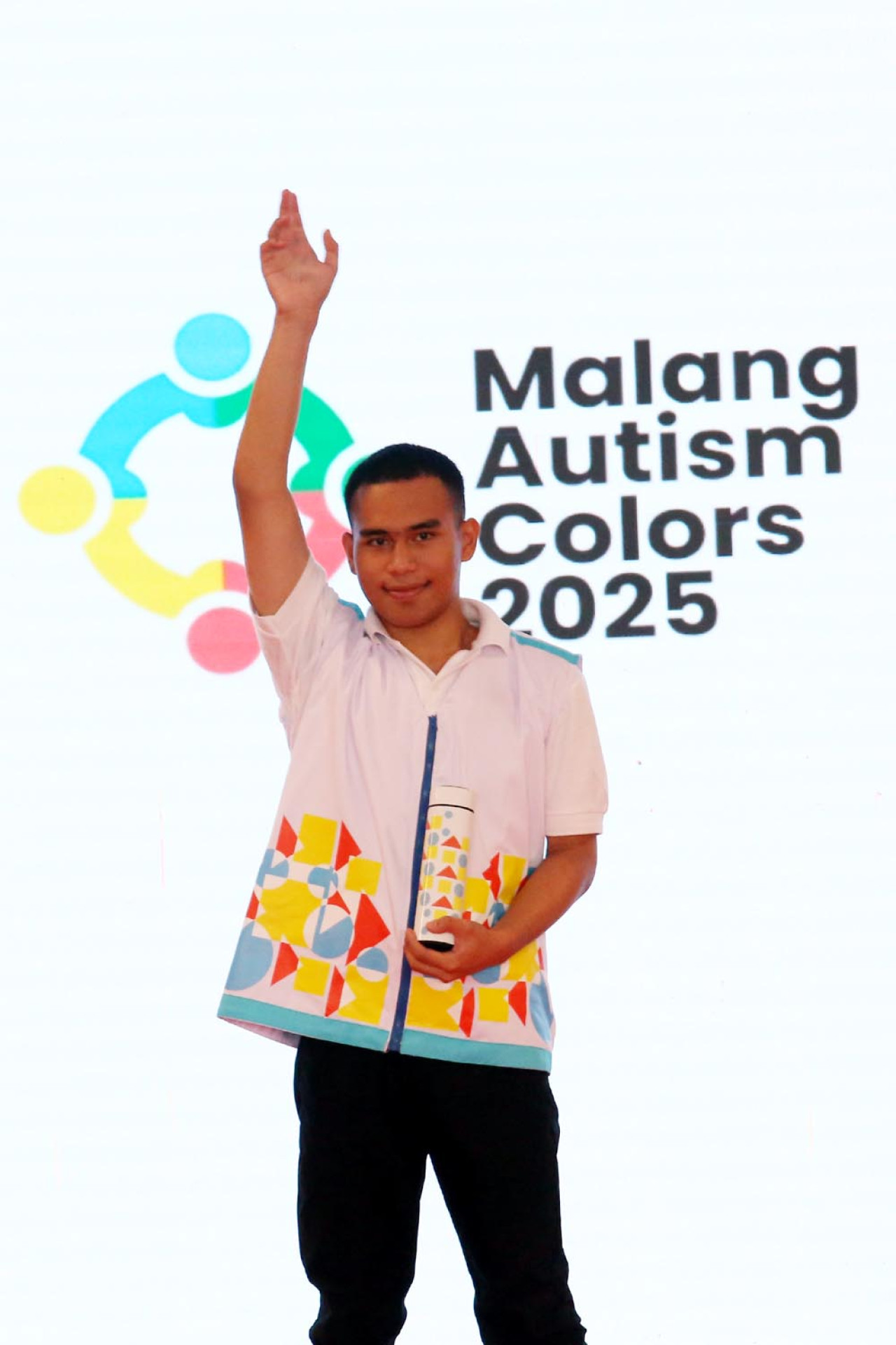 Seorang penyandang Autism Spectrum Disorder (ASD) melambaikan tangan dengan penuh percaya diri saat tampil sebagai model di fashion show Malang Autism Colors 2025 di MCC. Mengenakan kemeja putih beraksen warna cerah, penampilannya menjadi simbol keberhasilan MAC. (Foto: Ali Masduki/jatimnow.com)