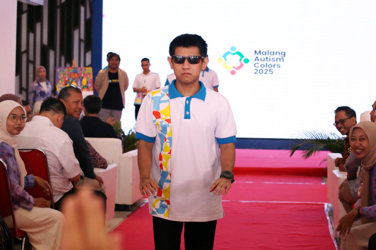 Salah satu penyandang ASD menunjukkan postur serius dan fokus saat tampil di fashion show Malang Autism Colors 2025 di MCC. Mengenakan polo shirt putih dengan aksen pola geometris, penampilannya disaksikan antusias oleh tamu undangan. (Foto: Ali Masduki/jatimnow.com)