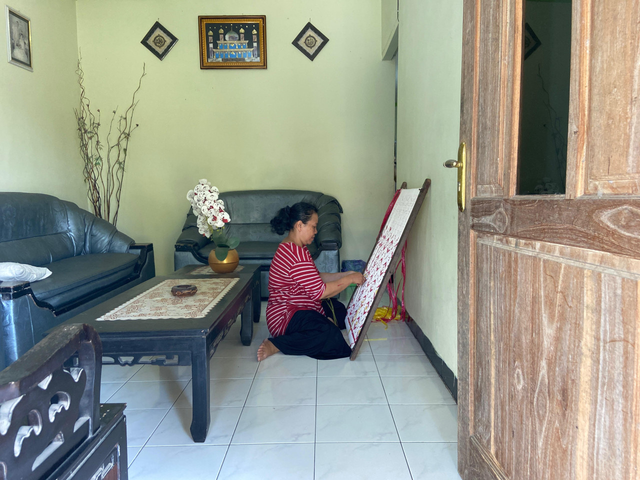 Umaha Tikum (53) sedang melakukan tahap pengikatan di rumahnya, tak jauh dari gerai Medali Mas 1. Pekerjaan ini sudah ia lakukan sejak lama. Dia lebih nyaman mengerjakan tahap ini daripada menenun. Di rumah, dia juga bisa sambil mengurus keluarga.