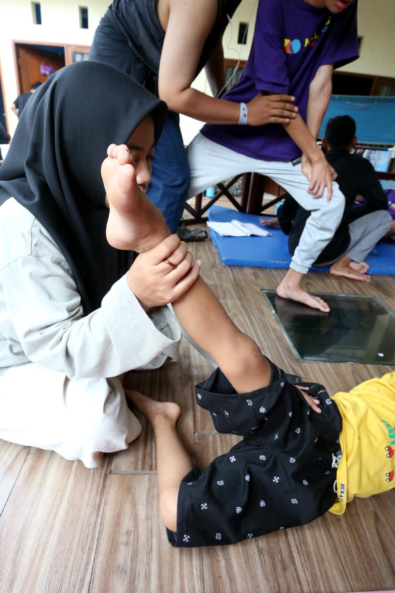 Seorang terapis dengan sabar membantu anak autisme melakukan latihan peregangan di Malang Autism Center. Gerakan sederhana ini melatih koordinasi dan kekuatan otot sekaligus membantu anak mengenali batas tubuhnya. (Foto: Ali Masduki/jatimnow.com)