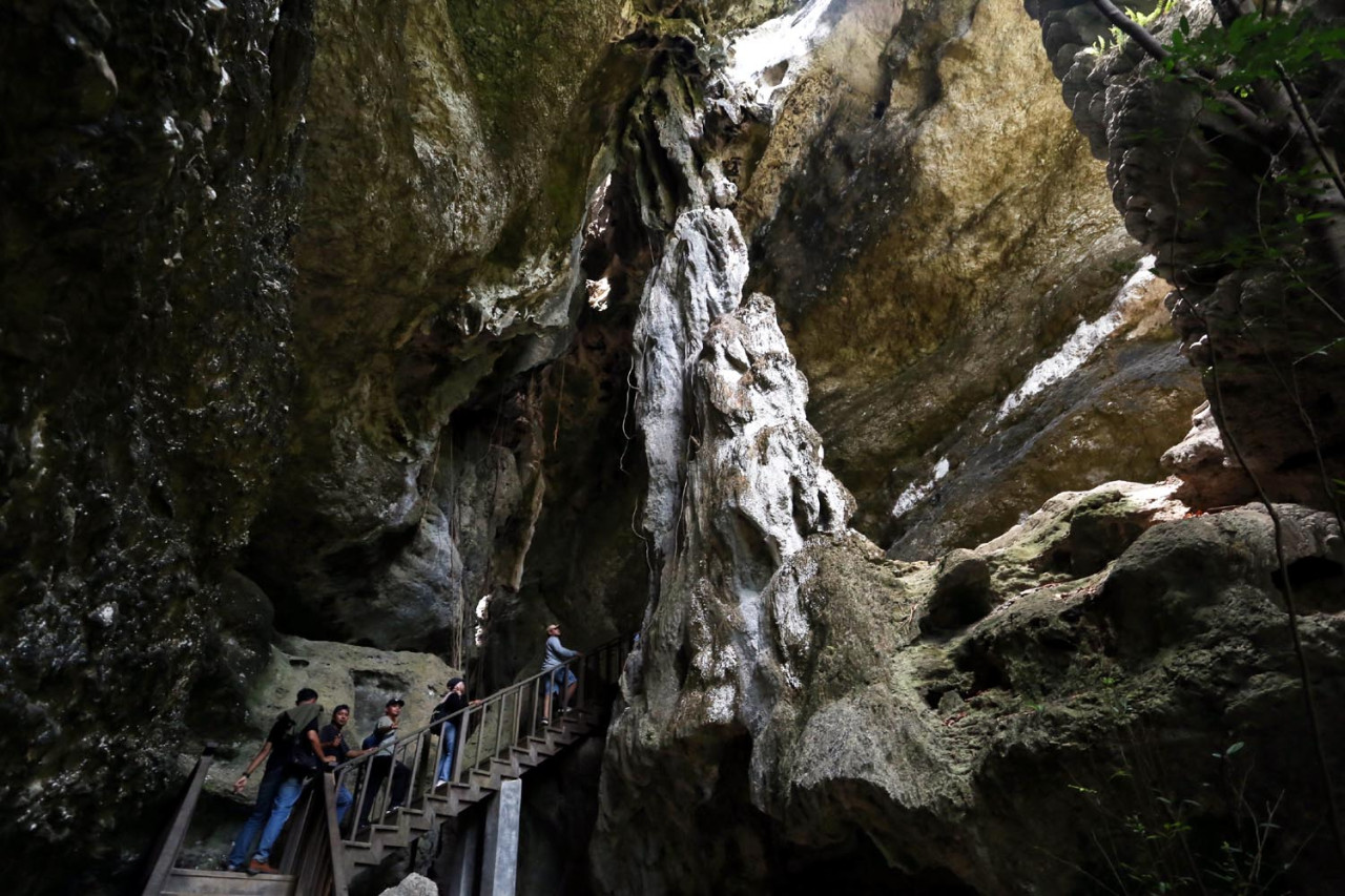 Tangga kayu menjadi penghubung antara dunia luar dan keajaiban di dalam Goa Batu Cermin, mengundang para pelancong untuk mengungkap rahasia yang tersimpan di dalamnya. (Foto: Ali Masduki/JatimNow.com)