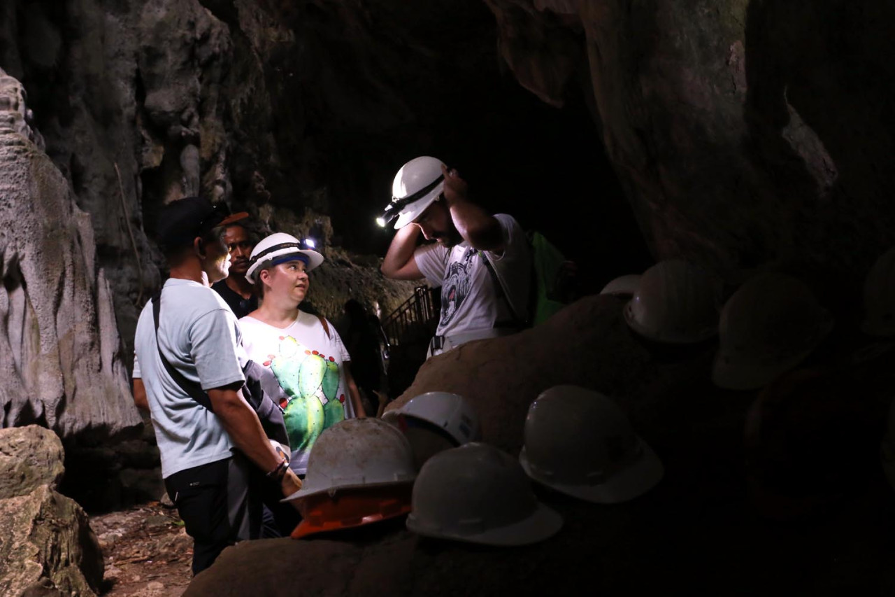 Dua wisatawan mancanegara mengenakan alat pelindung diri (APD) ketika akan masuk ke dalam salah satu ikon Goa Batu Cermin. (Foto: Ali Masduki/JatimNow.com)