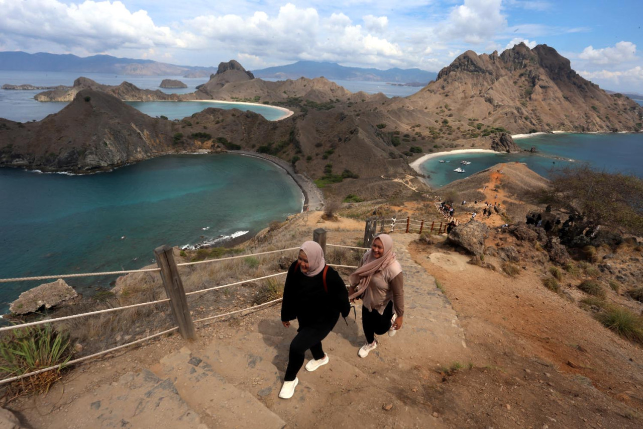 Dua wisatawan menikmati jalur pendakian menuju puncak Pulau Padar, Taman Nasional Komodo, Nusa Tenggara Timur. Dari titik tertinggi, terlihat jelas tiga teluk berwarna toska yang membentuk lanskap ikonik dan menjadi daya tarik utama destinasi ini. (Foto: Ali Masduki/JatimNow.com)