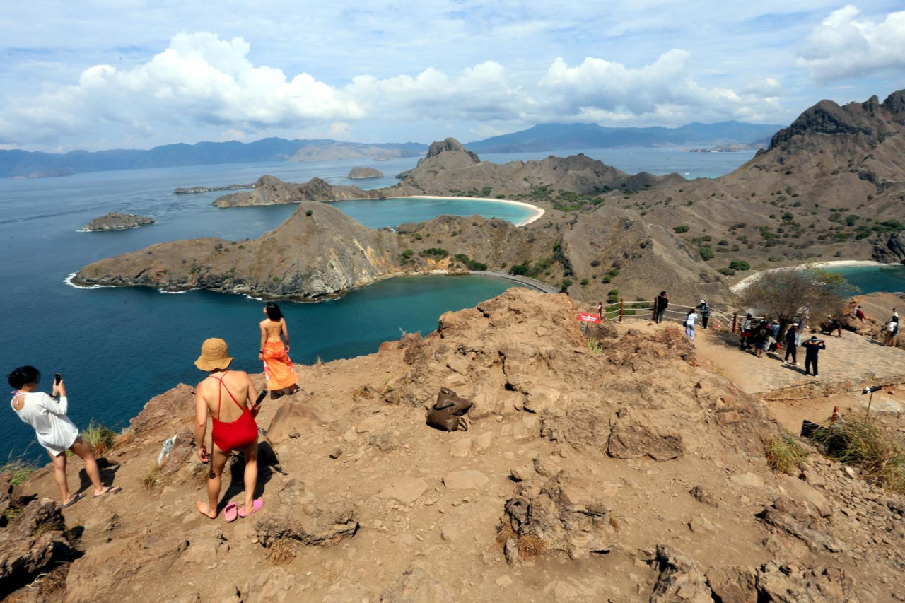 Pengunjung mengabadikan momen tak terlupakan di puncak Pulau Padar, dengan bukit-bukit dramatis dan air laut berwarna pirus yang membentang sejauh mata memandang. Taman Nasional Komodo menawarkan pengalaman yang tak terlupakan bagi pecinta alam dan pencari petualangan. (Foto: Ali Masduki/JatimNow.com)