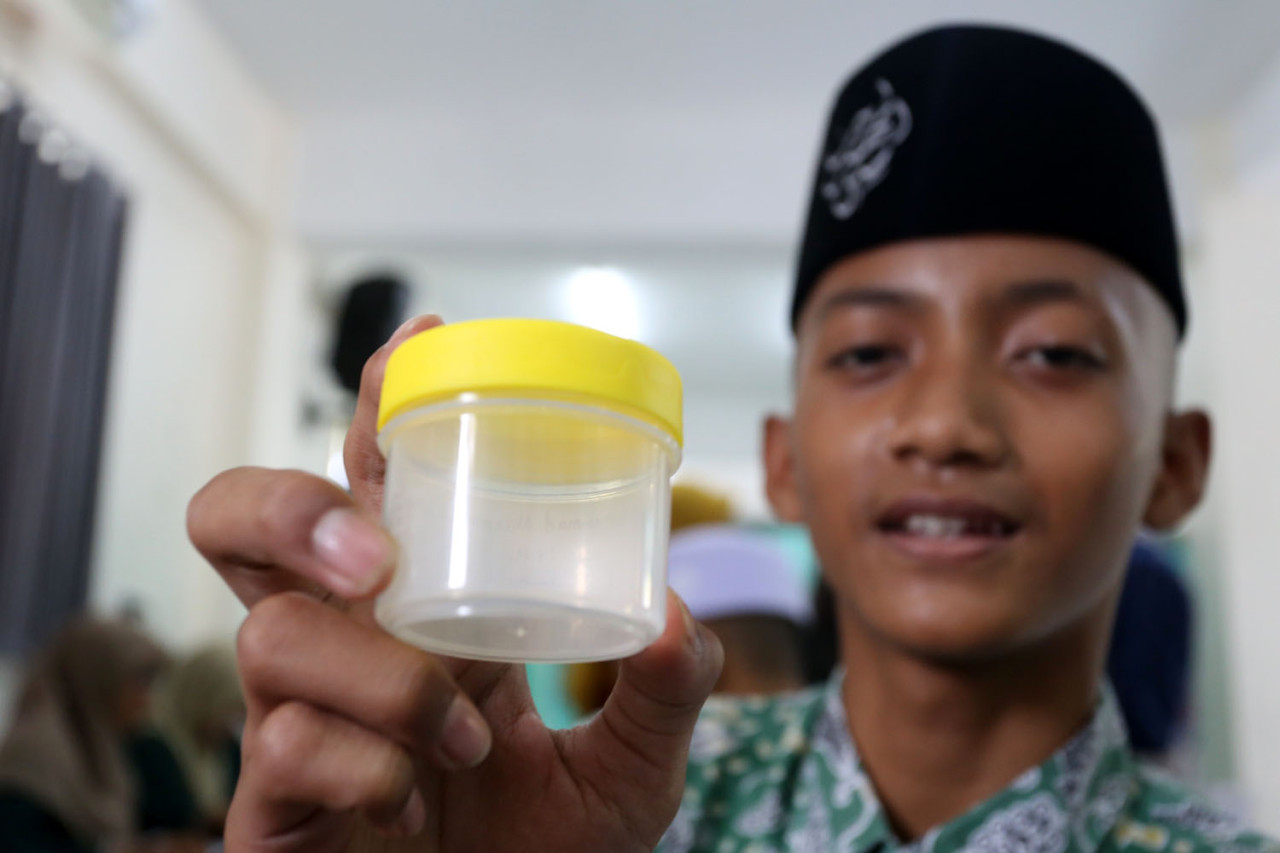 Seorang santri Pondok Pesantren Modern Sunanul Muhtadin, Gresik, menunjukkan wadah sampel pemeriksaan sebagai bagian dari Program Cek Kesehatan Gratis (CKG), Kamis (18/12/2025). Pemeriksaan ini mendukung deteksi dini penyakit, termasuk Tuberkulosis (TB), guna menjaga kesehatan santri di lingkungan pesantren yang beraktivitas secara komunal.(Foto: Ali Masduki/jatimnow.com)