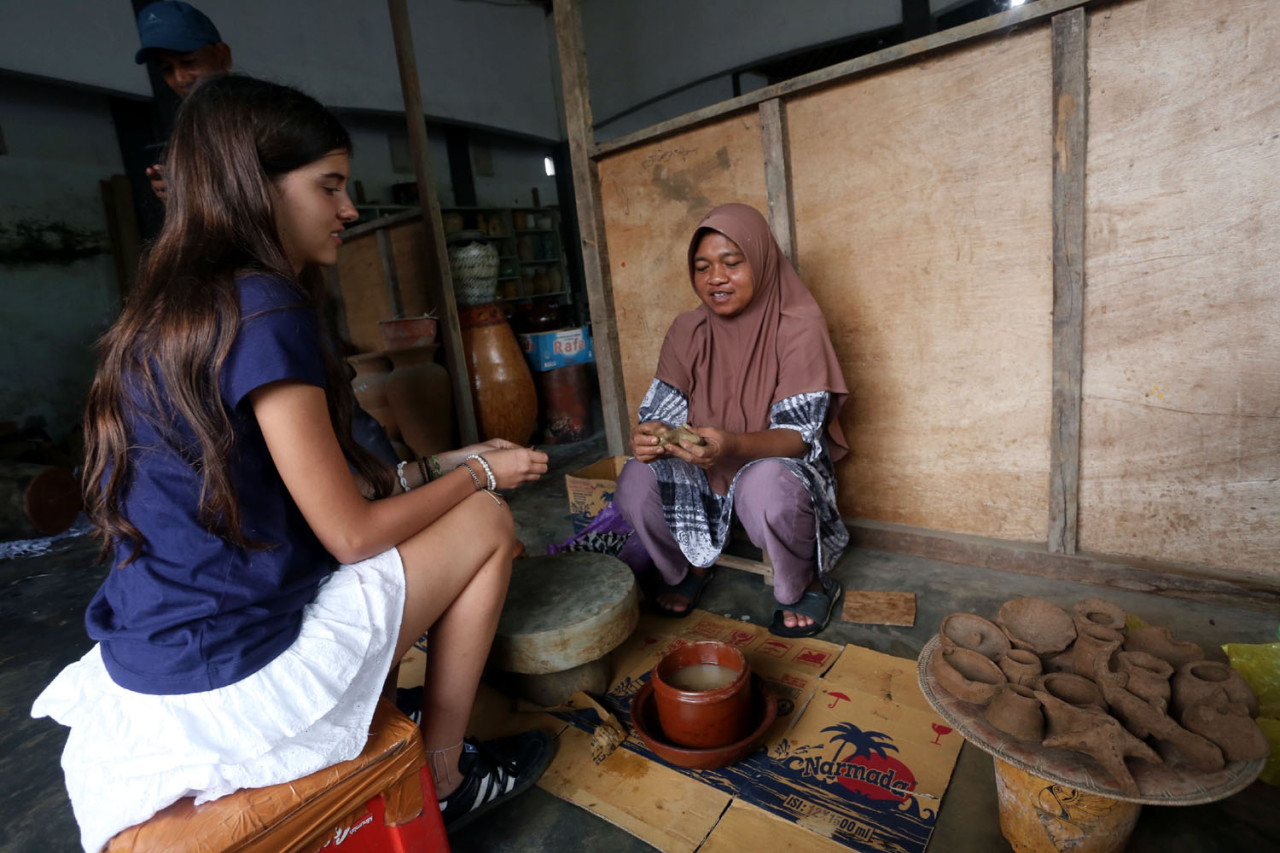 Seorang turis mancanegara berbincang sambil belajar membentuk gerabah bersama pengrajin di Desa Banyumulek, Lombok Barat, Sabtu (27/12/2025). Di ruang sederhana, proses berbagi cerita dan keterampilan tradisional ini menjadi pengalaman berharga yang mempertemukan budaya lokal dengan rasa ingin tahu wisatawan dunia. (Foto: Ali Masduki/jatimnow.com)