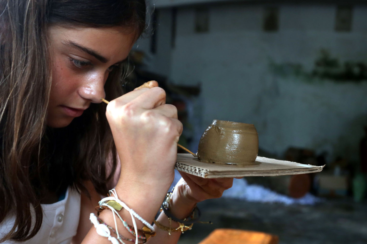 Seorang turis mancanegara dengan penuh ketelitian merapikan detail gerabah khas Banyumulek, Lombok Barat, Sabtu (27/12/2025). Dari sentuhan tangan sederhana ini, terlihat bagaimana kerajinan tradisional mampu memikat wisatawan dunia lewat pengalaman budaya yang otentik dan bermakna. (Foto: Ali Masduki/jatimnow.com)
