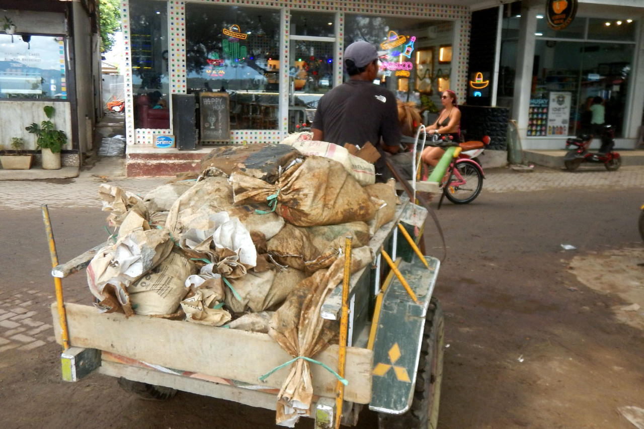 Cidomo, kendaraan tradisional tanpa mesin mengangkut karung-karung material bangunan menyusuri jalan utama Gili Trawangan. Di pulau bebas kendaraan bermotor ini, distribusi bahan bangunan bergantung pada tenaga manusia dan hewan, menambah panjang ongkos dan beratnya proses pembangunan di kawasan wisata.(Foto: Ali Masduki/jatimnow.com)