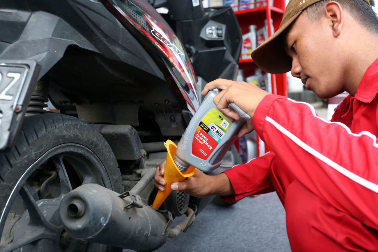 Seorang petugas menuangkan pelumas Enduro ke sepeda motor milik pengemudi ojek online saat layanan servis oli gratis yang diselenggarakan Pertamina Patra Niaga di SPBU COCO Jemursari, Surabaya, Rabu (24/12/2025). Program ini merupakan bagian dari Enduro Entrepreneurship Program sebagai bentuk apresiasi dan dukungan terhadap para driver ojol agar kendaraan tetap terawat dan siap menunjang aktivitas harian. (Foto: Ali Masduki/jatimnow.com)