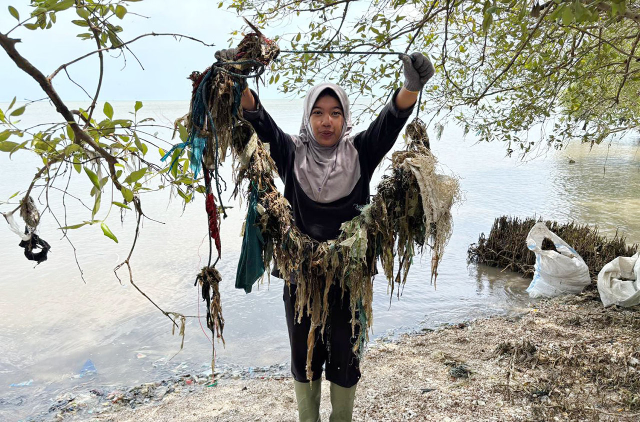 Seorang relawan menunjukkan tumpukan sampah plastik yang berhasil dilepas dari jeratan mangrove di pesisir Wonorejo, Surabaya, dalam aksi bersih lingkungan untuk melindungi ekosistem mangrove dari ancaman kerusakan dan mikroplastik. (Foto: Ecoton/jatimnow.com)