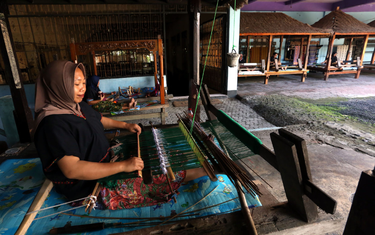 Seorang perempuan penenun di Desa Sukarara, Lombok Tengah, dengan sabar menyusun benang pada alat tenun tradisional, merekam aktivitas harian masyarakat Sasak yang menjaga keberlangsungan warisan tenun songket khas Lombok. (Foto: Ali Masduki/jatimnow.com)