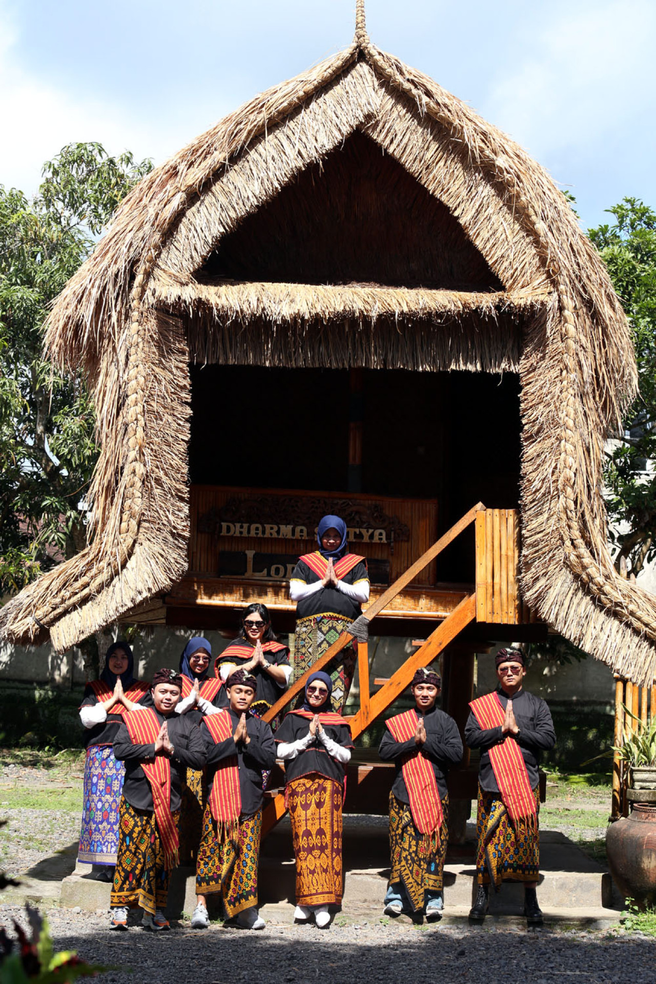 Sekelompok wisatawan mengenakan busana adat tenun khas Sasak foto bersama di rumah tradisional beratap alang-alang, Desa Sukarara, Lombok Tengah. (Foto: Ali Masduki/jatimnow.com)