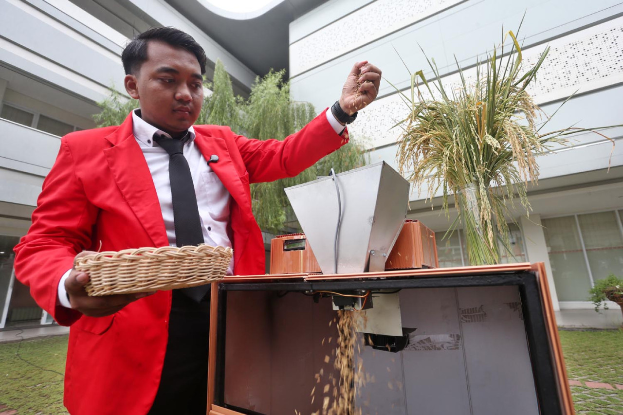 Nur Ahmad Justine Ivana menunjukkan cara kerja alat pemisah dan pengering padi otomatis di Untag Surabaya, Senin (09/2/2026). (Foto: Ali Masduki/jatimnow.com)
