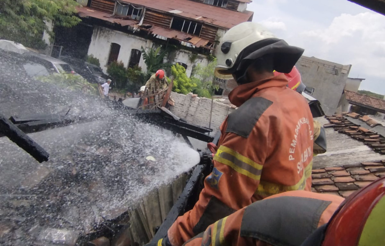 Petugas dari DPKP Kota Surabaya melakukan pembasahan rumah semi permanen yang terbakar di Jalan Bumiarjo Gang V No. 41-B, Kelurahan Sawunggaling, Kecamatan Wonokromo, Sabtu (7/3/2026). (Foto: DPKP Kota Surabaya for jatimnow.com)