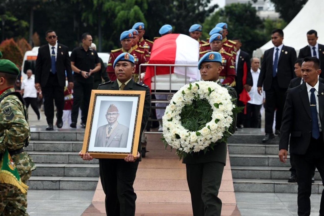 Prajurit TNI membawa foto dan karangan bunga di depan peti jenazah Wakil Presiden RI ke-6, Try Sutrisno, yang diselimuti Bendera Merah Putih dalam prosesi pemakaman militer di Jakarta, Senin (2/3/2026). Sejumlah pejabat negara dan keluarga mengantar kepergian mantan Panglima ABRI tersebut. (Foto: Tim Media Presiden)