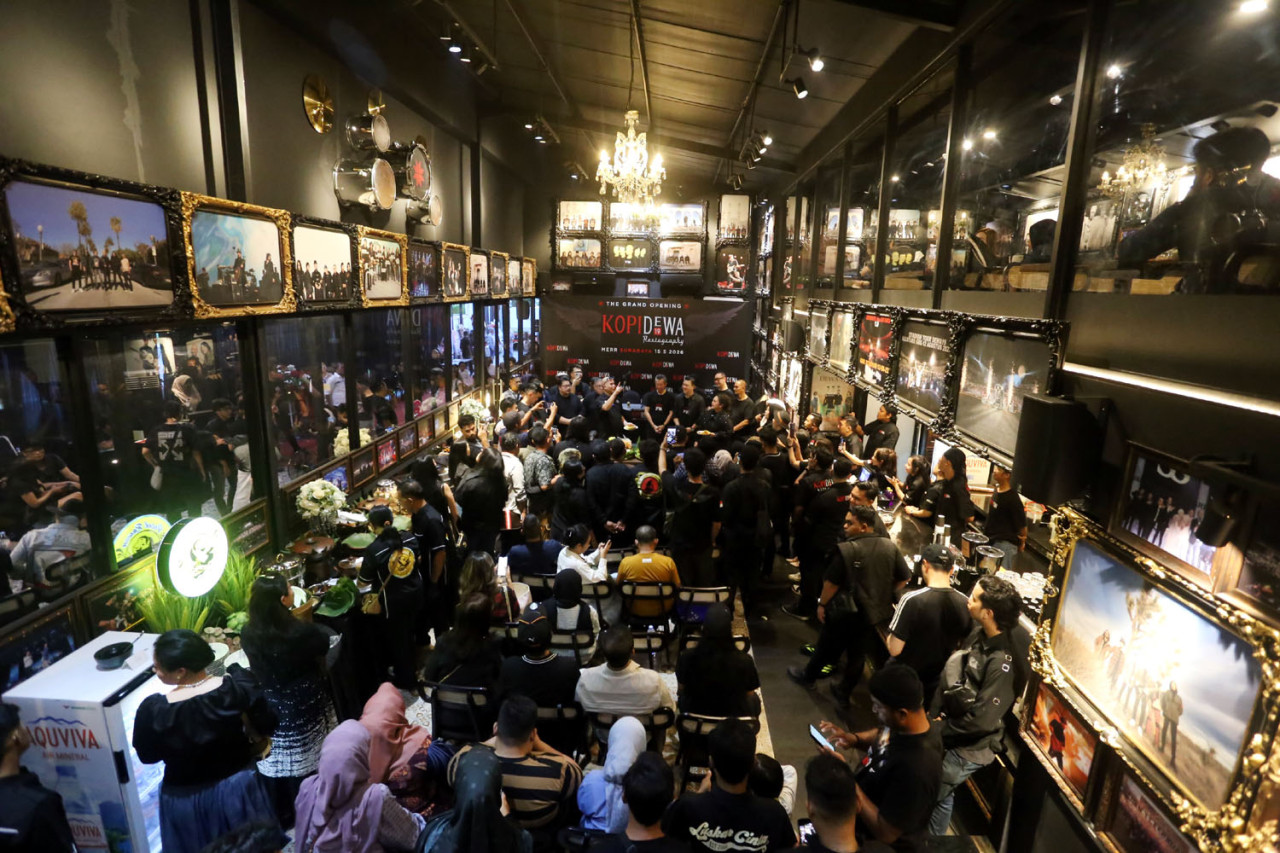 Suasana grand opening Kopi Dewa 19 MERR Surabaya dipenuhi Baladewa, Jumat (15/5/2026). Interior kafe dihiasi foto perjalanan Dewa 19 dan berbagai memorabilia band yang menghadirkan nuansa nostalgia bagi pengunjung. (Foto: Ali Masduki/jatimnow.com)