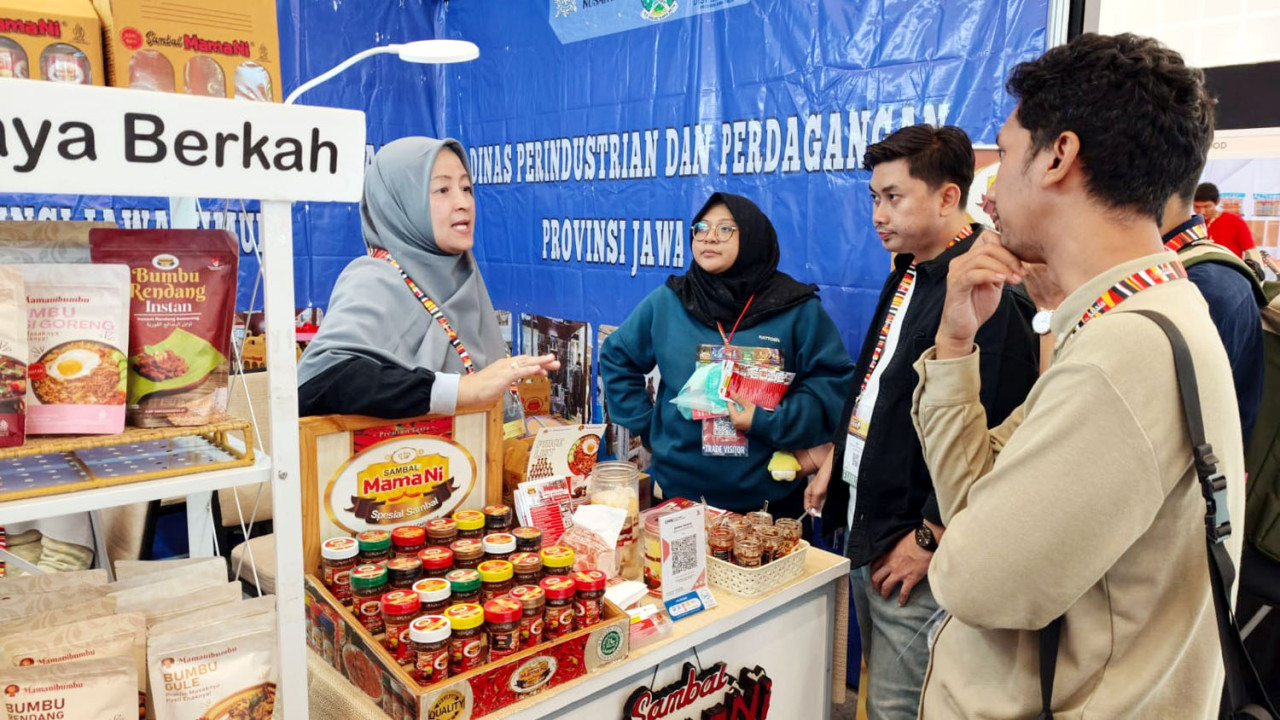 Heni Wardhani sibuk melayani pengunjung di stan Disperindag Jatim dalam gelaran IIFEX 2026 di Grand City Convention Hall Surabaya, Sabtu (20/6/2026) malam. (Foto: Ali Masduki/jatimnow.com)
