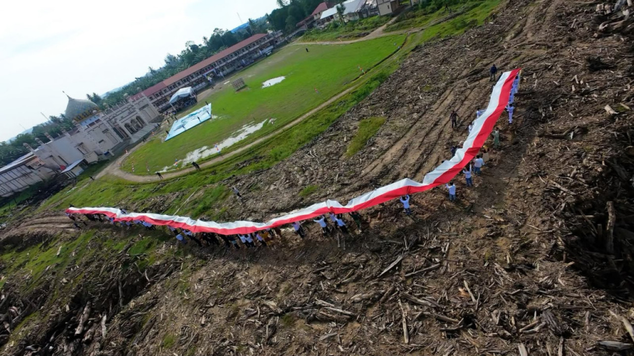 Pengibaran bendera raksasa ini menjadi bagian dari program Relawan Bakti BUMN (RBB) 2026 bertema “Menyemai Harapan di Tanah Tamiang”. (Foto: BSI for jatimnow.com)