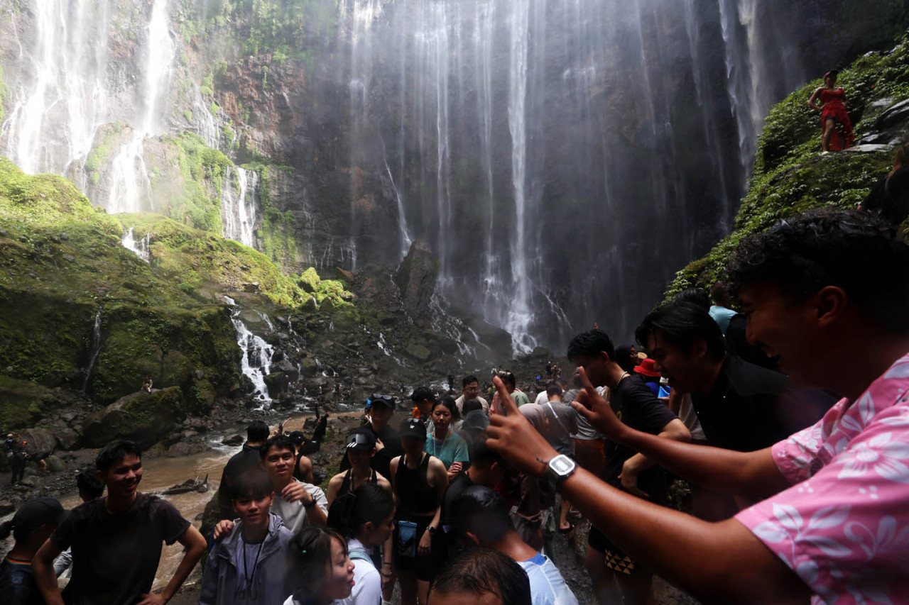 Wisatawan memadati destinasi wisata Air Terjun Tumpak Sewu di Kabupaten Lumajang, Jawa Timur. Mereka rela antri untuk sekedar foto di atas batu dengan latar belakang aliran air yang jatuh dari tebing membentuk tirai raksasa.(Foto: Ali Masduki/jatimnow.com)