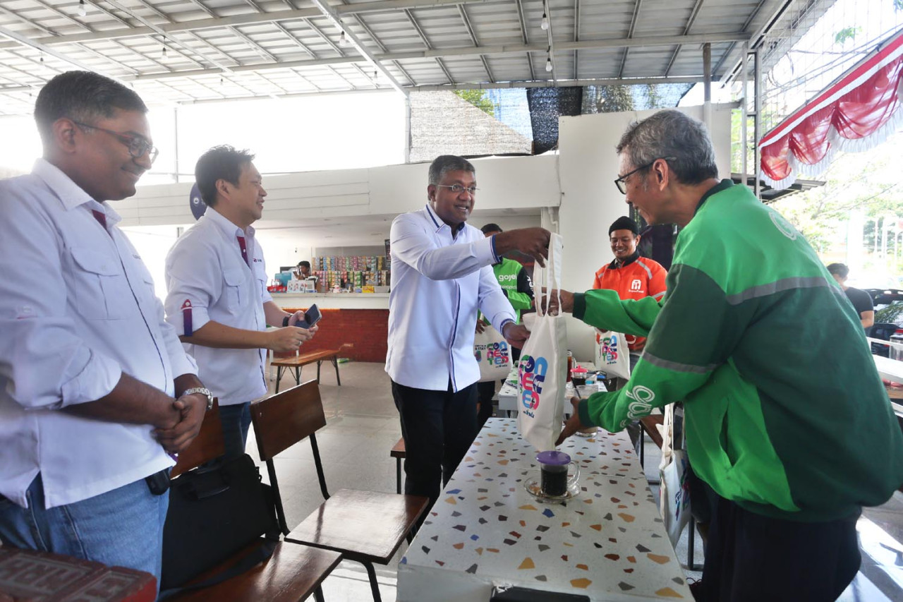 Direktur sekaligus Chief Technology Officer XLSMART, Shurish Subbramaniam, menyerahkan souvenir usai berdialog dengan sejumlah mitra pengemudi di Warkop Titik Kumpul, Jalan Jawa, Kamis (03/9/2026). (Foto: Ali Masduki/jatimnow.com)