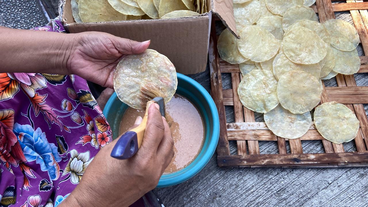 Maimunah mengoleskan bumbu pada kepingan emping di kawasan Kampung Emping Belinjo, Kecamatan Pare, Kabupaten Kediri, Kamis (8/10/2026). Dia merupakan pelopor emping dengan varian rasa udang pedas, udang pedas manis, dan bawang manis. (Foto: Yanuar Dedy/jatimnow.com)