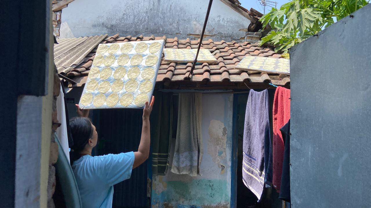 Ida Kristiani (49) menjemur emping di bagian belakang rumahnya di Koplakan, Kecamatan Pare, Kabupaten Kediri, Kamis (8/10/2026). Papan yang masing-masing berisi 25 keping emping itu ia tata di atas atap kamar mandi rumahnya. Sejumlah perempuan yang telah berkeluarga mengerjakan sebagian proses produksi emping dari rumah masing-masing. Pola kerja tersebut memungkinkan mereka tetap menjalankan pekerjaan rumah tangga sekaligus memperoleh penghasilan dari produksi emping. (Foto: Yanuar Dedy/jatimnow.com)
