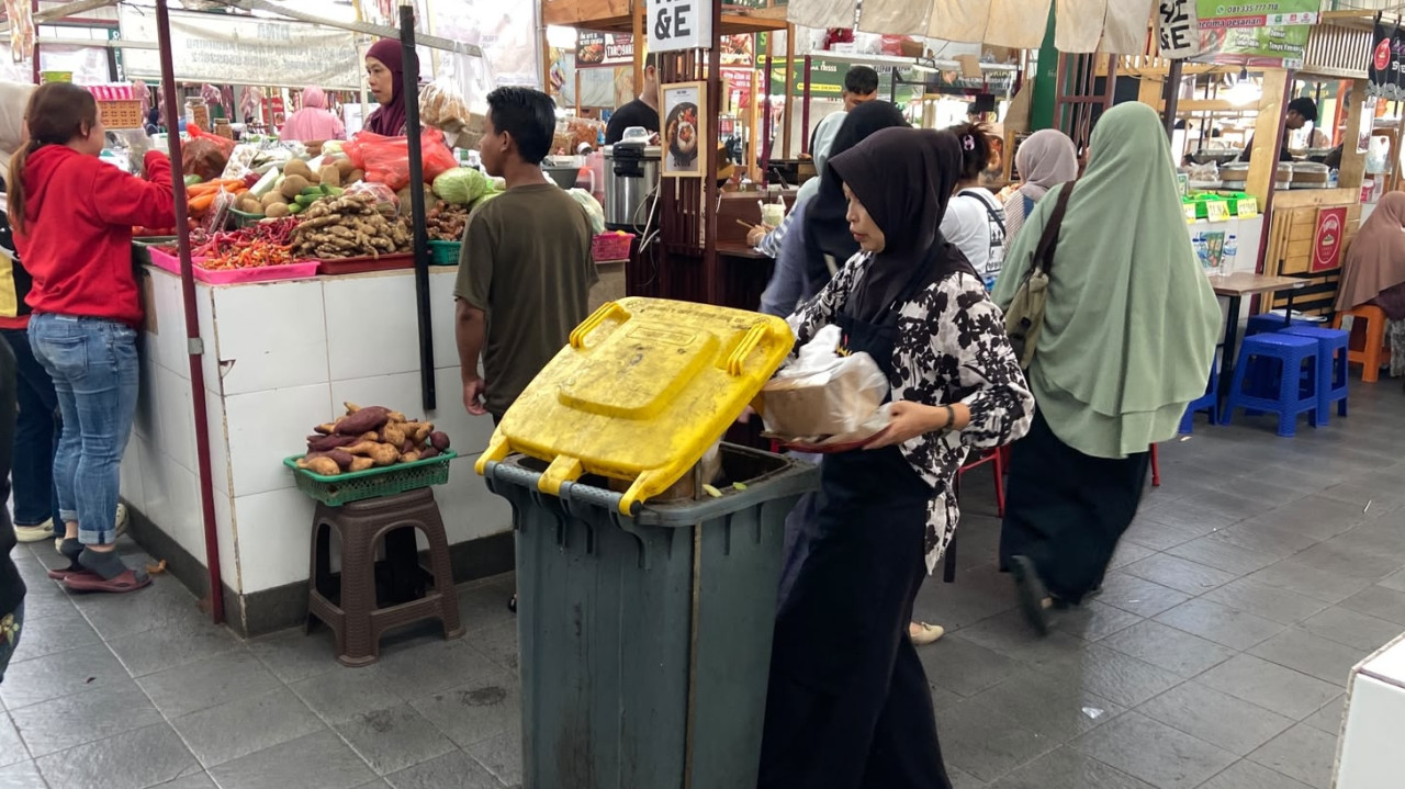 Pedagang membuang sampah di tempat sampah yang tersedia di setiap lorong Pasar Rakyat Klojen Nikmat, Sabtu (23/10/2026). Fasilitas dan kebiasaan baik ini membuat pasar terasa sangat bersih. (Foto: Yanuar Dedy/jatimnow.com)