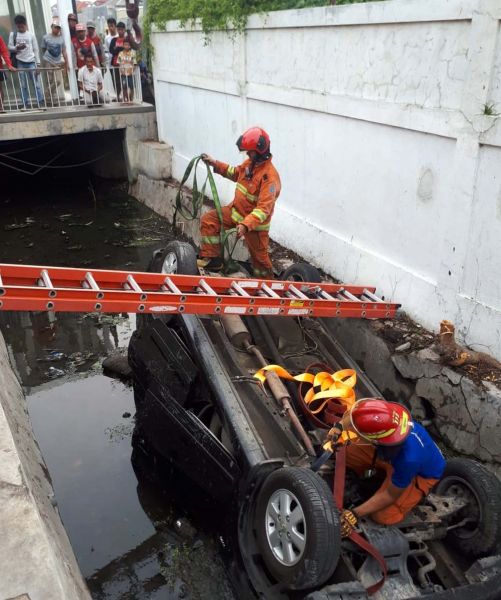 Petugas PMK Surabaya mengevakuasi mobil yang terperosok dan terbalik di selokan