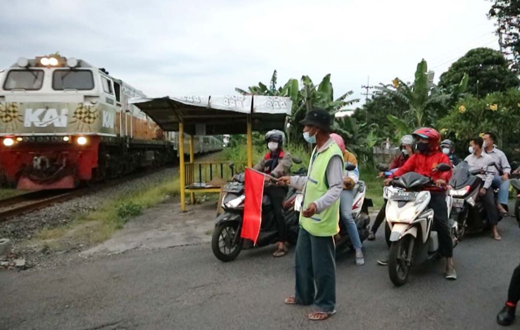 Kesi, saat menghentikan laju kendaraan yang akan melintas rel kereta api tanpa palang pintu di Surabaya
